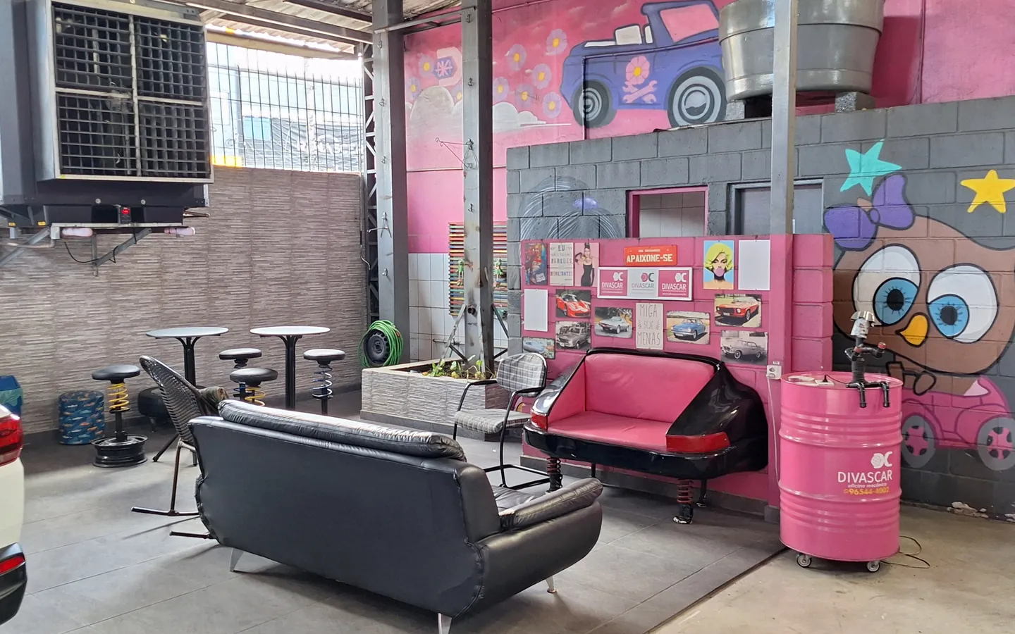 Sala de espera dentro da oficina, com sofás, mesas e parede grafitada
