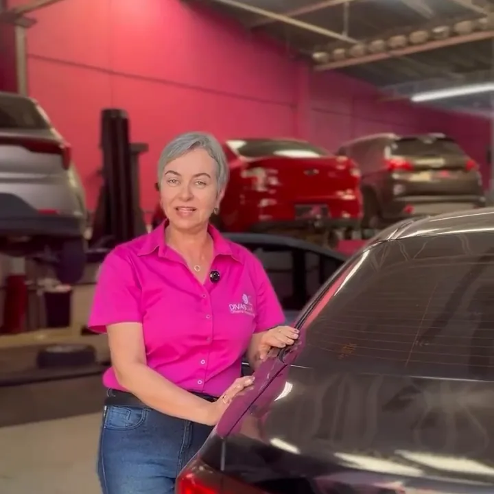 A Joelma, dona da Divas Car, na oficina, com carros nos elevadores atrás